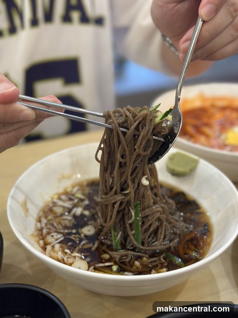 Noodles being lifted with spoon and chopsticks