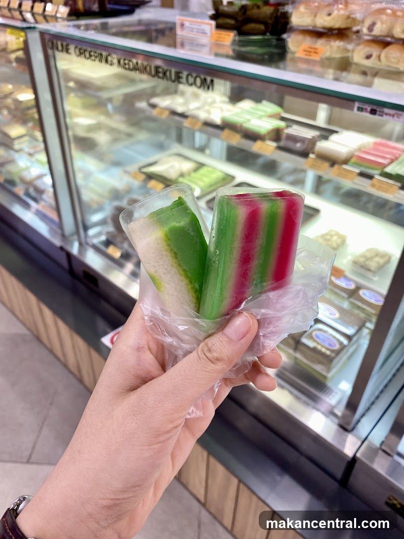 Hand holding kueh sticks in front of display case