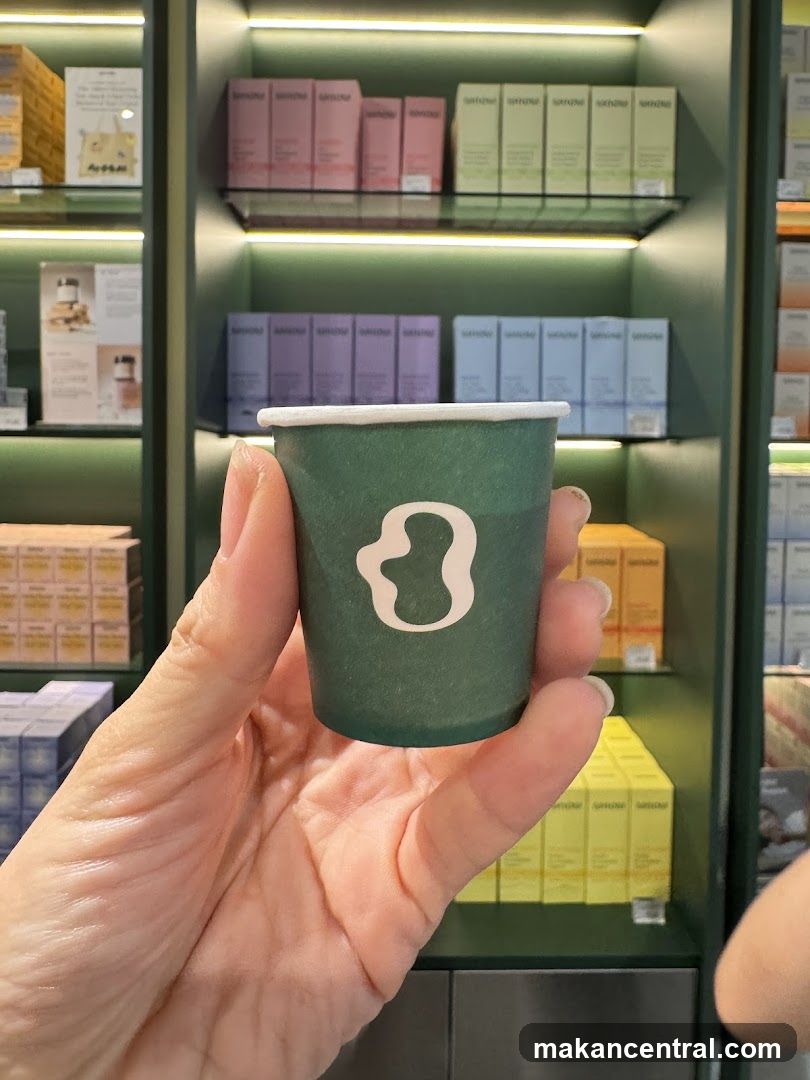 Hand holding a small green cup with a white logo in front of shelves of products