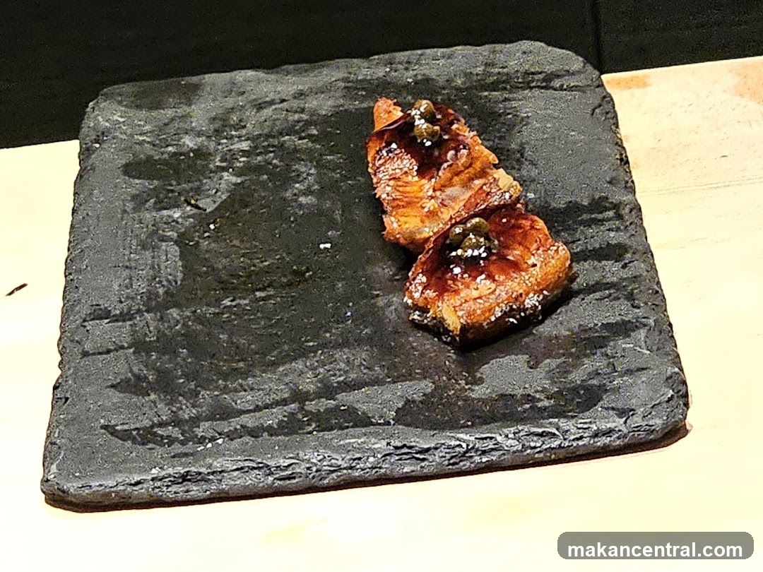 Two pieces of glazed food on a dark stone plate
