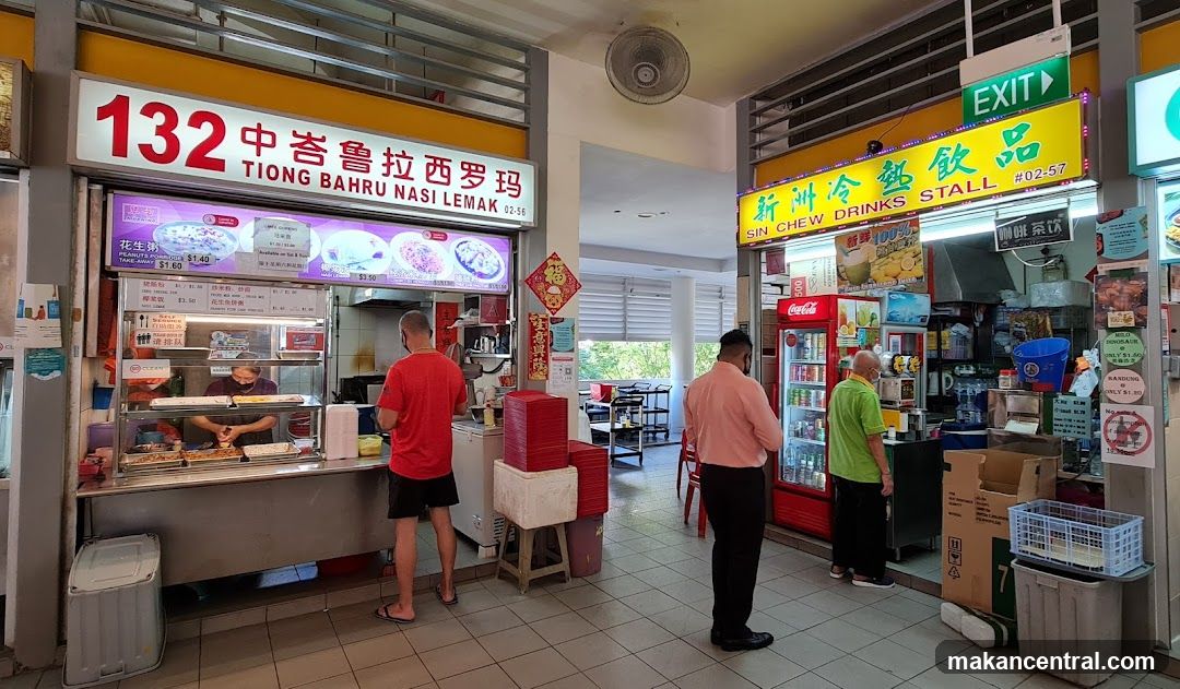 A food stall with a prominent sign for "132 TIONG BAHRU NASI LEMAK" and another stall next to it labeled "SIN CHEW DRINKS STALL". Both stalls are open with staff serving customers. The nasi lemak stall displays images of its dishes and prices. The drinks stall has a refrigerator stocked with beverages and a menu board.