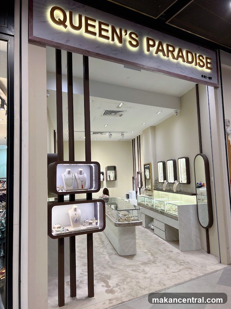 The exterior of a jewelry store called Queen's Paradise. The store has a clean and modern design with marble accents and warm lighting. Display cases inside showcase various jewelry pieces.