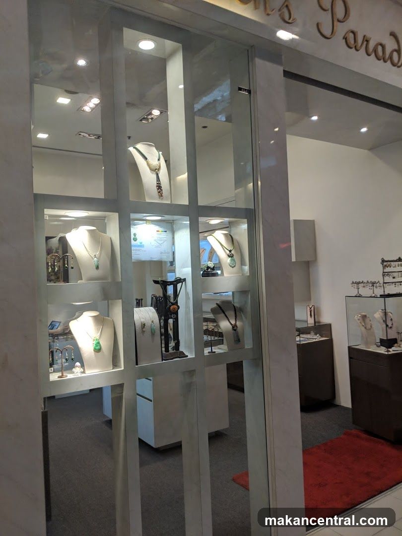 A storefront window display for a jewelry store, showcasing various necklaces and earrings on mannequins and stands. The store's name, "Jewelry's Paradise", is visible in gold lettering above the display. The interior of the store is visible through the window, with display cases and furniture.