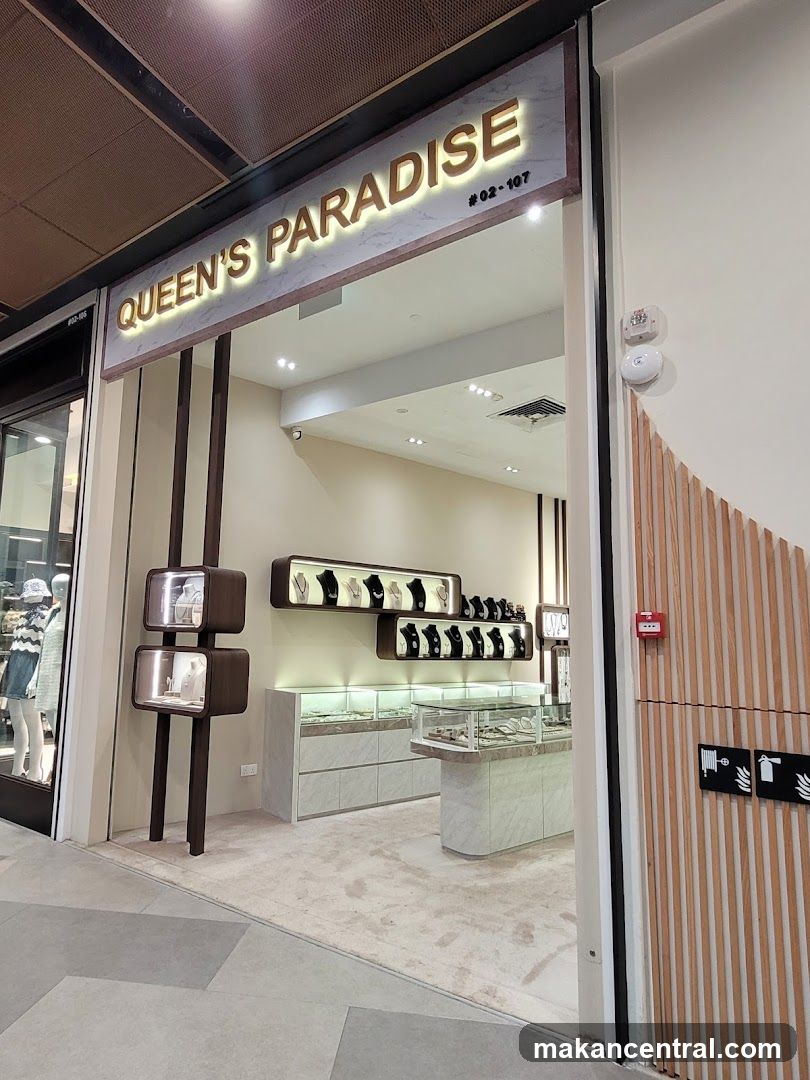 The exterior of a jewelry store called Queen's Paradise. The store has a marble facade with illuminated gold lettering. Inside, display cases showcase jewelry, and shelves on the wall hold necklaces.