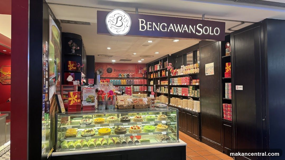 A well-lit shop front with a display of cakes and pastries in a refrigerated case. Shelves behind the counter are stocked with various packaged goods, likely cookies and snacks. A prominent sign above the entrance reads "BENGAWAN SOLO".