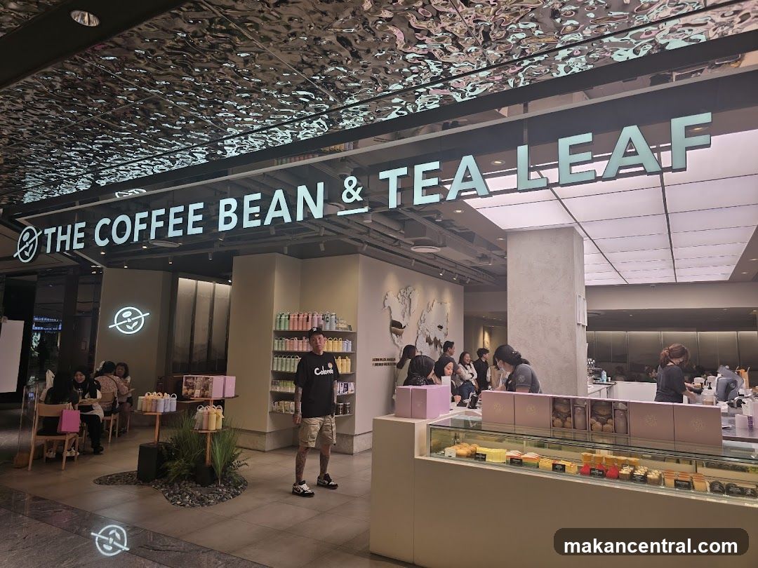 A man stands in front of a brightly lit storefront for The Coffee Bean & Tea Leaf. The store features a large sign with the company name, a display case with pastries, and shelves stocked with merchandise. Several customers are seated inside the cafe.