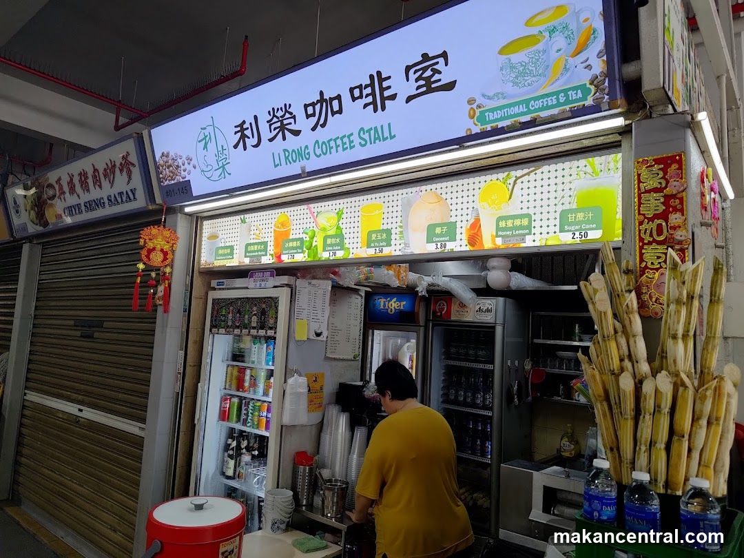 A coffee stall with a large illuminated sign displaying the stall name in English and Chinese, along with images of drinks and the text "TRADITIONAL COFFEE & TEA". Below the sign is a display of drinks and fresh sugarcane. A person is visible behind the counter. To the left, another stall sign for "CHYE SENG SATAY" is partially visible.