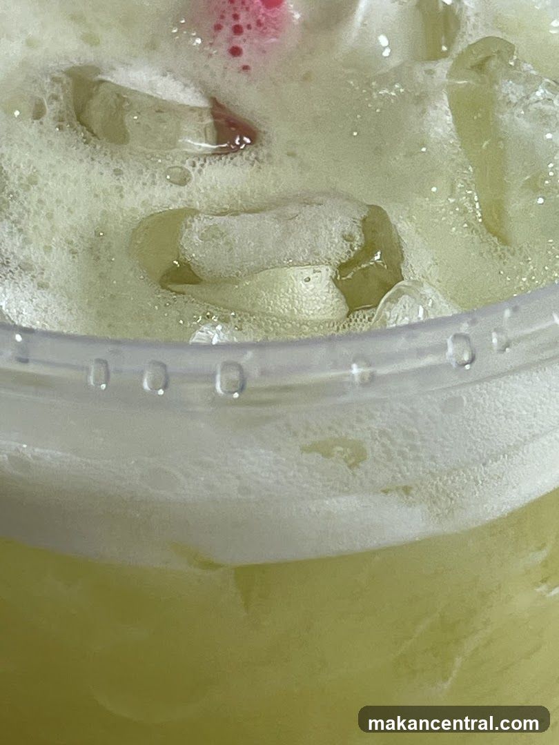 Close-up of a frothy green beverage with ice
