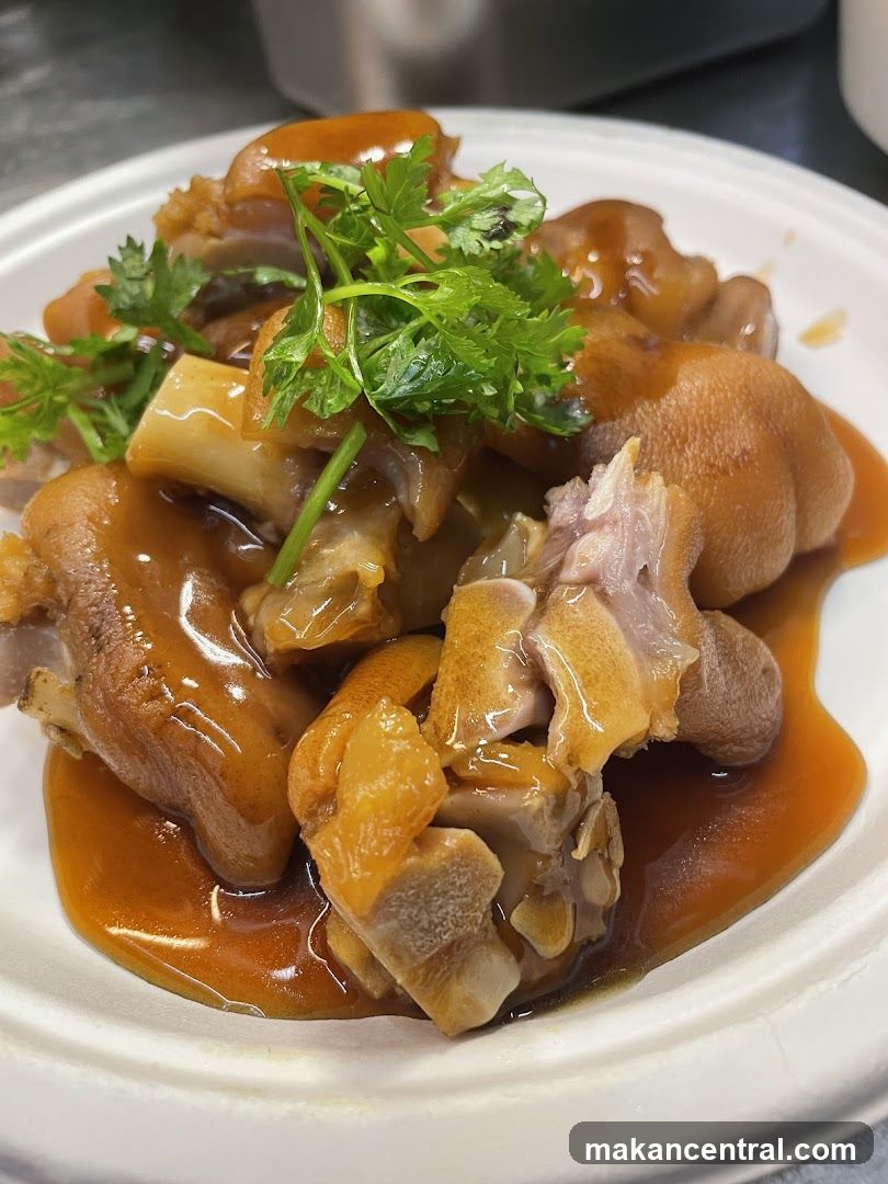 A close-up shot of braised pig feet in a rich, glossy sauce, garnished with fresh cilantro. The dish is served in a white disposable bowl.