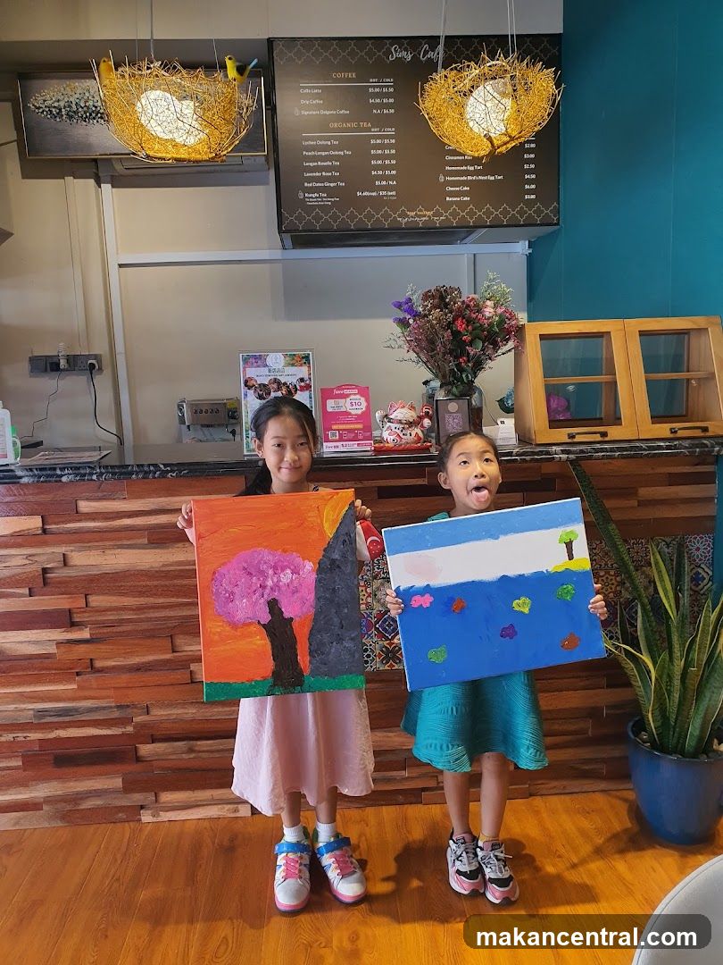Two girls holding up paintings in a cafe