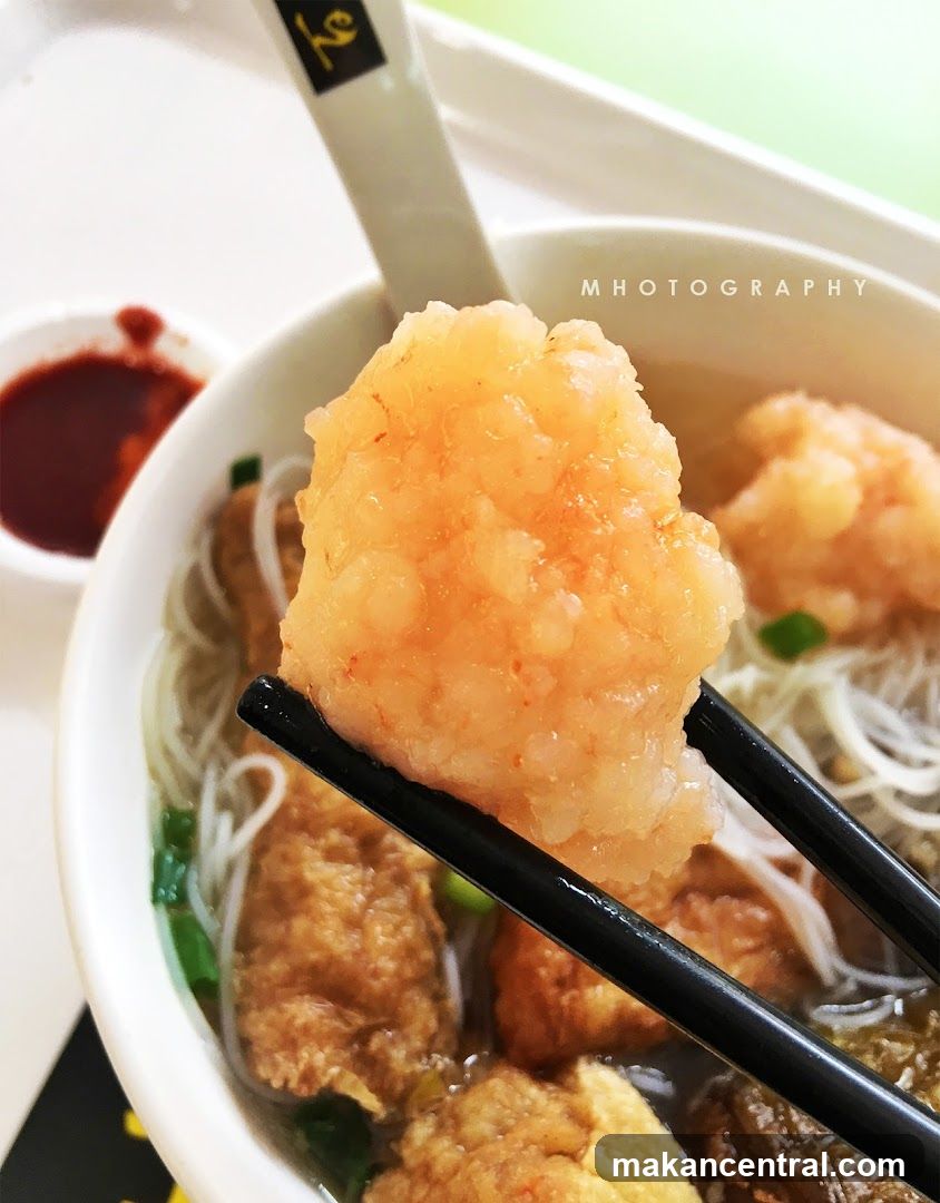 Close-up of a bowl of noodle soup with a large piece of shrimp being held by chopsticks.