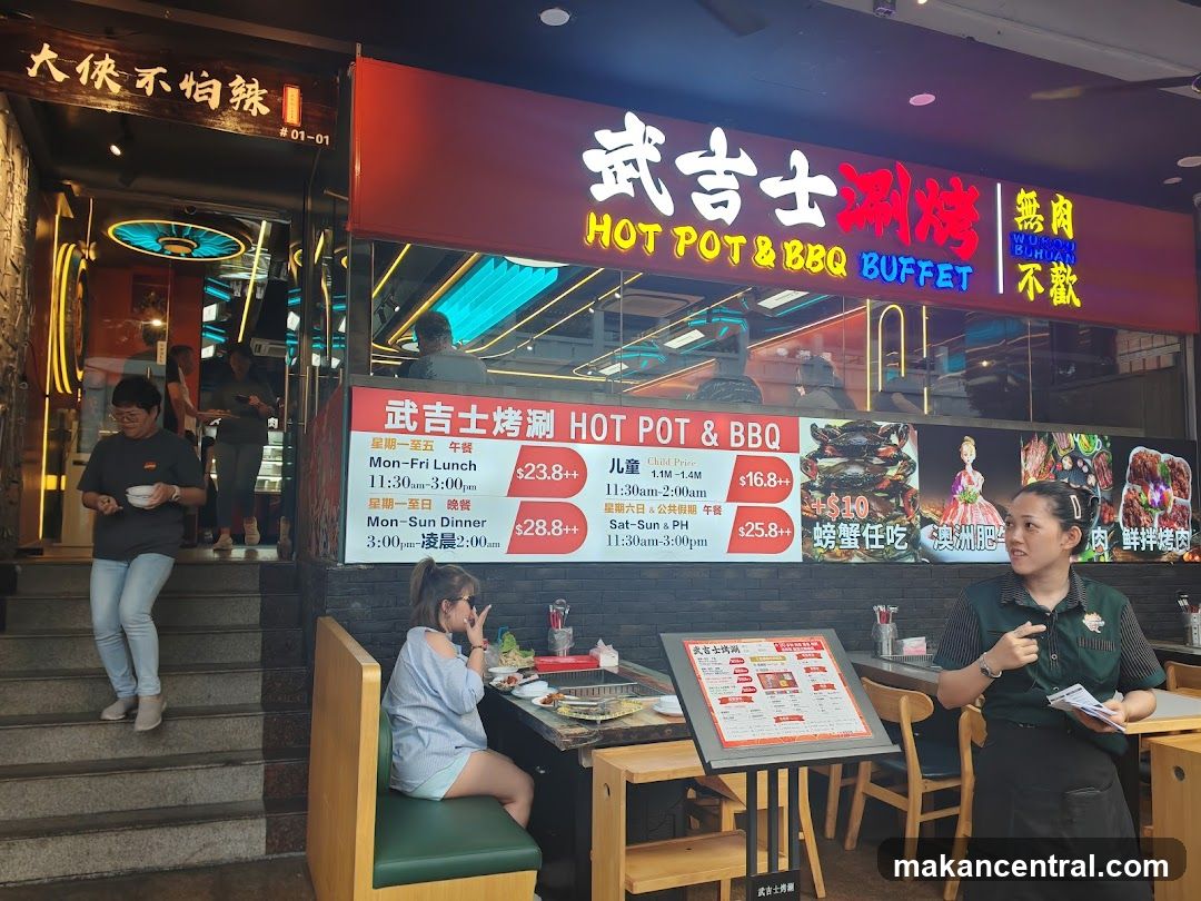 The exterior of a restaurant with a prominent neon sign that reads "HOT POT & BBQ BUFFET" in English and Chinese. Below the main sign, a menu board displays prices and times for lunch and dinner. People are seen entering and exiting the establishment.