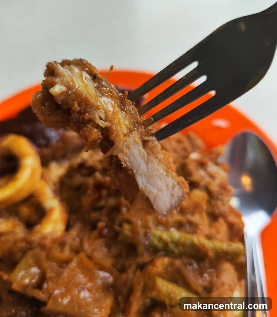 Close-up of a fork lifting a piece of breaded meat from a dish.