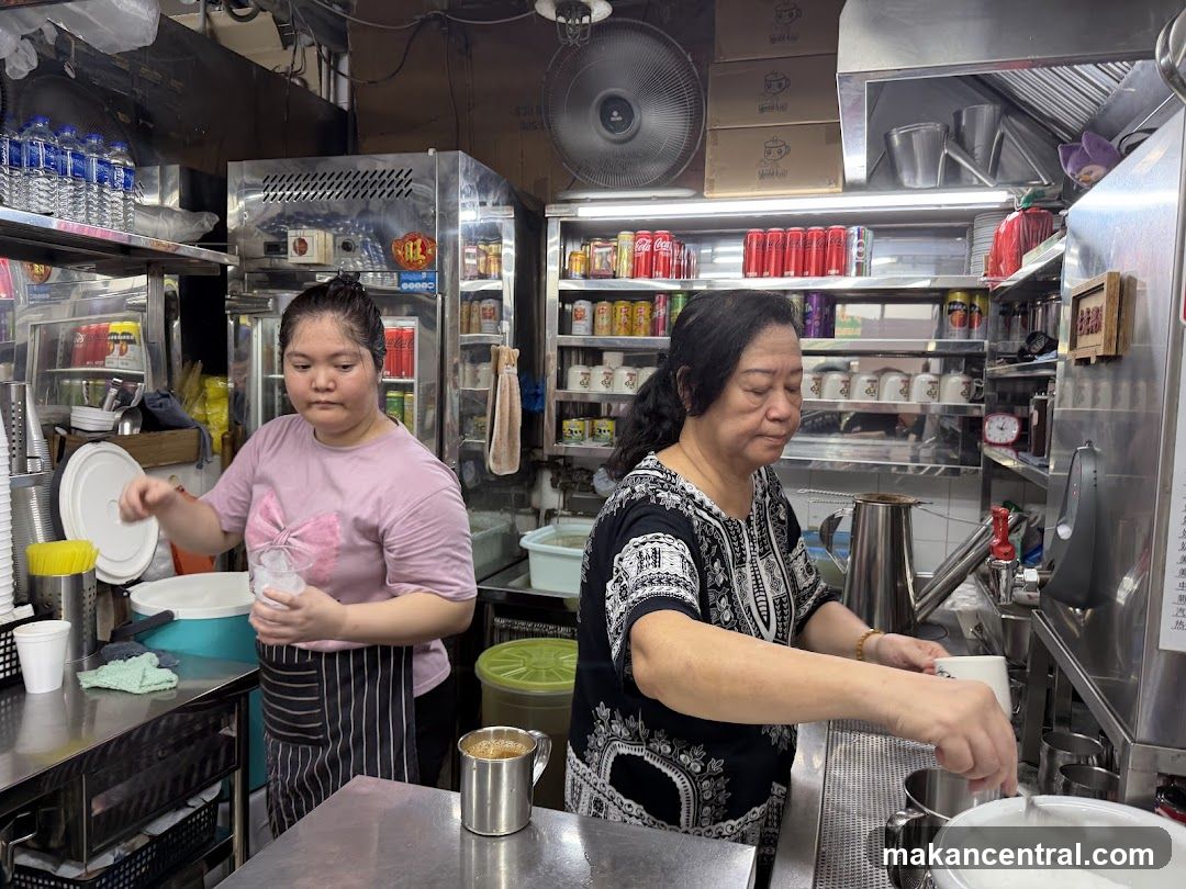 Two women preparing drinks in a busy food stall