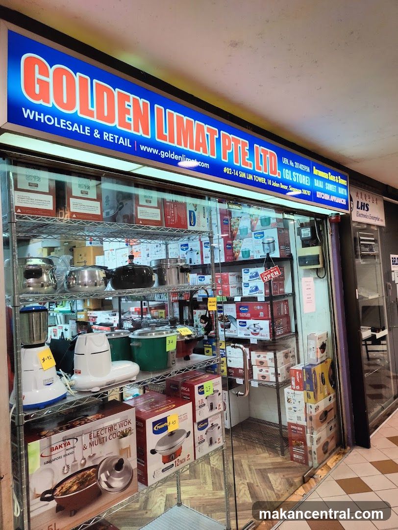 The storefront of Golden Limat Pte. Ltd., a wholesale and retail store. The store displays various kitchen appliances and cookware on shelves behind a glass window. The signage above the store reads "GOLDEN LIMAT PTE. LTD." with the website "www.goldenlima.com" below it. Other signs indicate the store's address and some of the brands they carry, such as Bajaj and Sumee.
