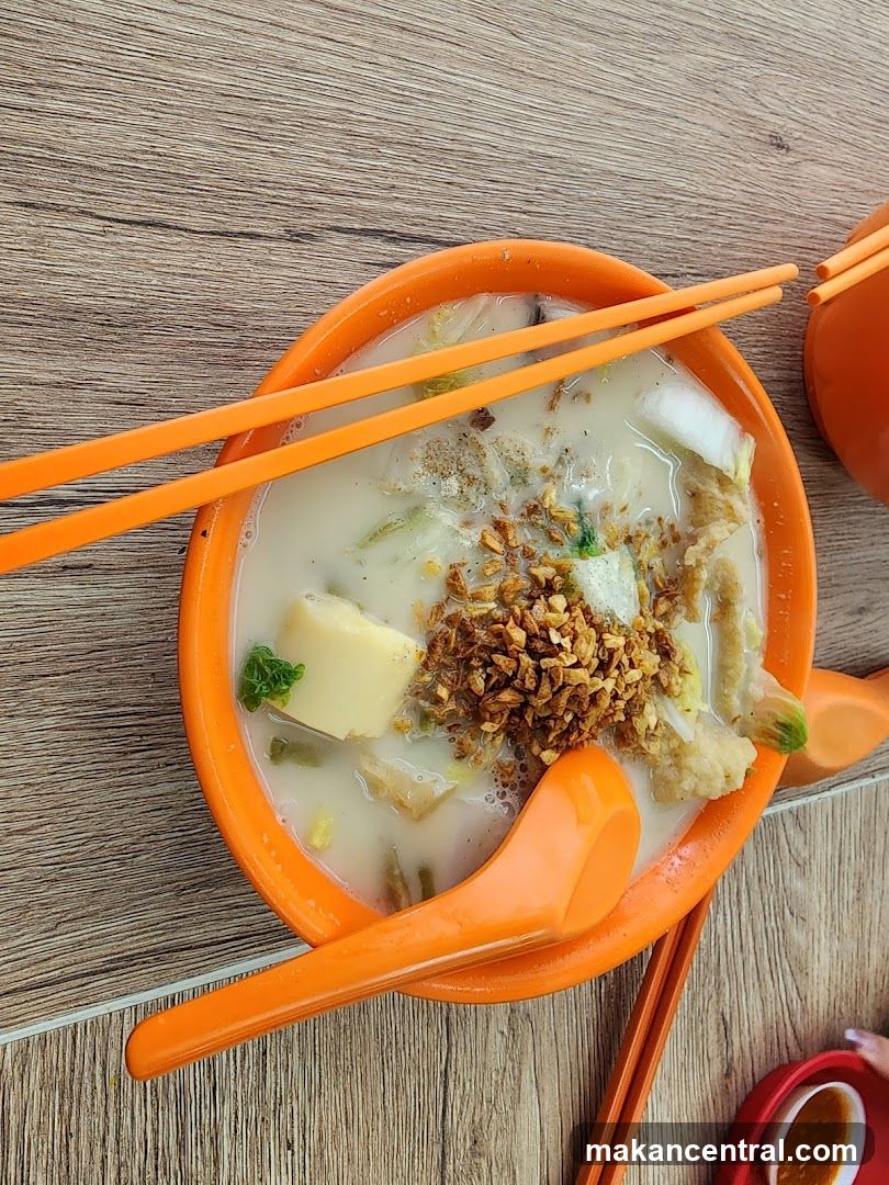 Orange bowl of soup with chopsticks and spoon