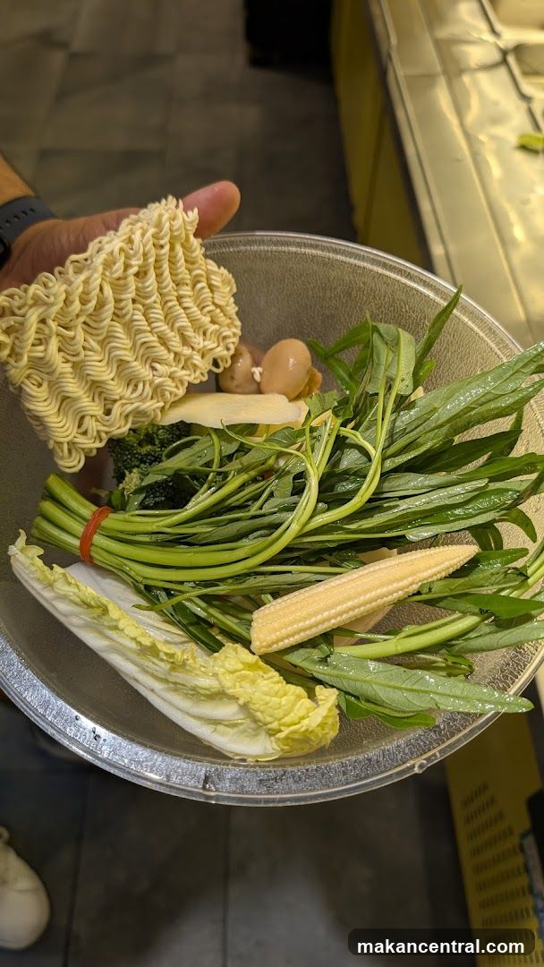 Hand holding instant noodles over a bowl of vegetables