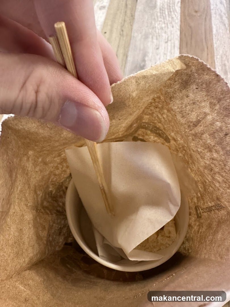Hand holding chopsticks over paper bag with cup inside