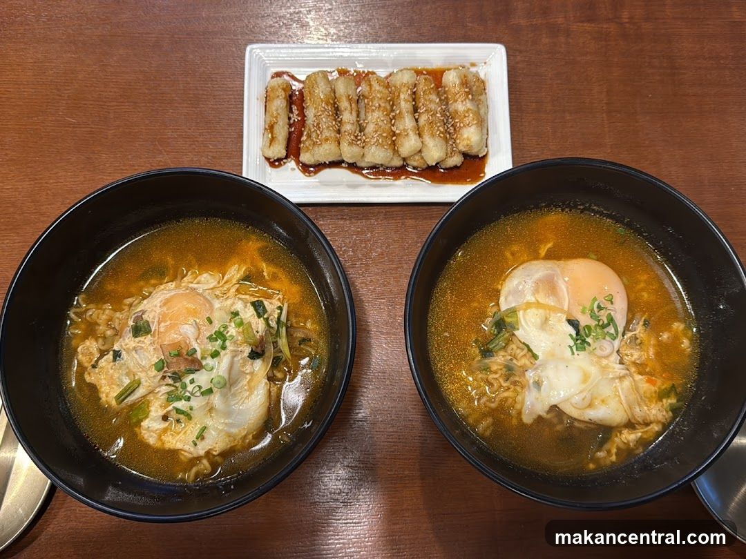Two bowls of ramen with eggs and a side of fried snacks