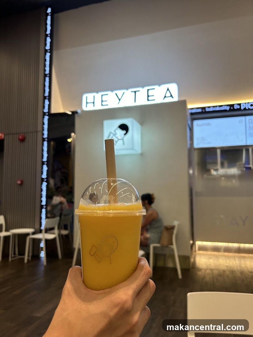 Person holding a mango smoothie in front of a Heytea store