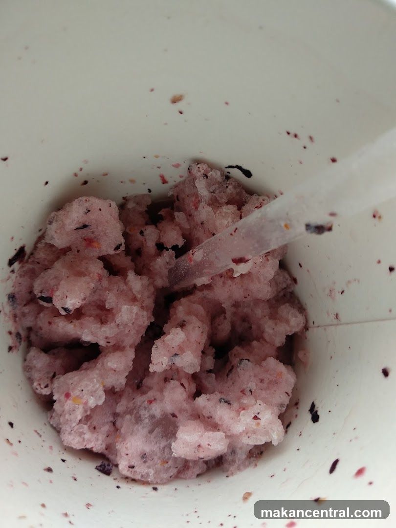 Close-up of a berry-flavored shaved ice in a white cup with a straw.