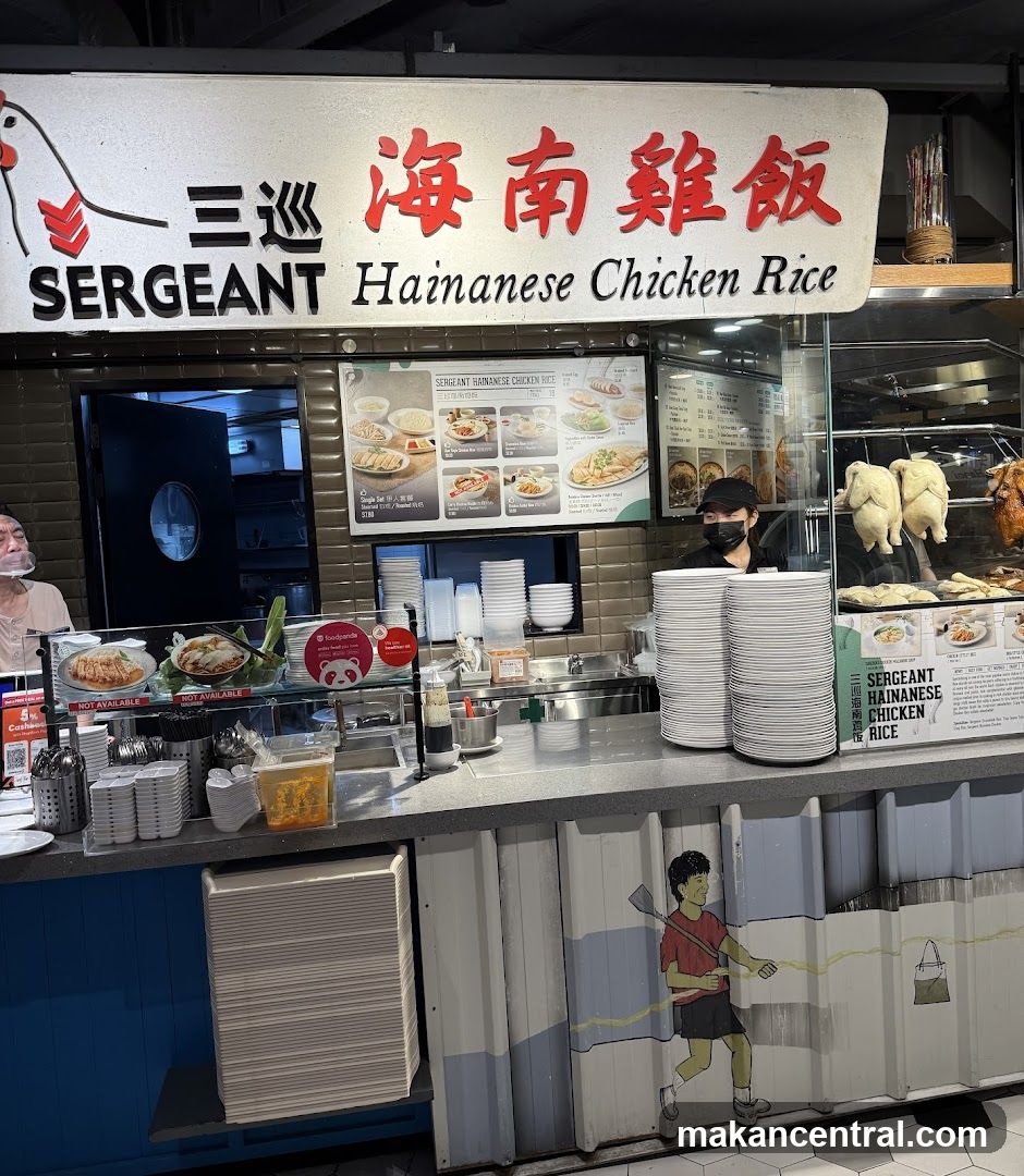A food stall with a large sign displaying "SERGEANT Hainanese Chicken Rice" in English and Chinese. The stall features a menu board with pictures of dishes, stacks of plates, and a display of roasted chickens. A staff member wearing a mask is visible behind the counter.