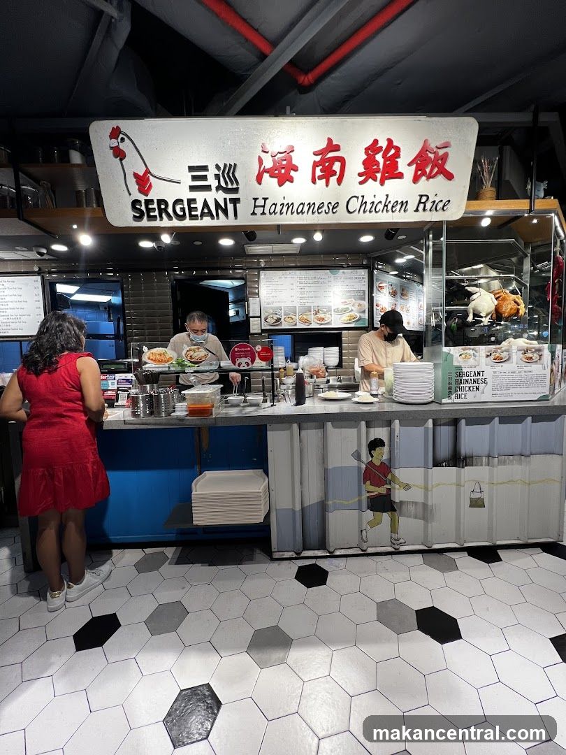 A food stall with a sign that reads "SERGEANT Hainanese Chicken Rice" in English and Chinese. There are two staff members behind the counter, and a customer is standing in front of the counter. The stall displays pictures of food and a whole roasted chicken. The floor has a hexagonal tile pattern.