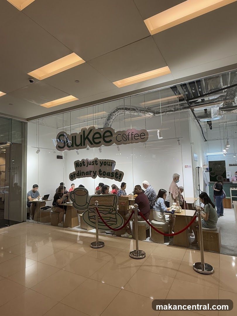 The exterior of a coffee shop with large glass windows. Inside, customers are seated at tables. A large graphic of pancakes and a coffee cup is visible. The shop's name,