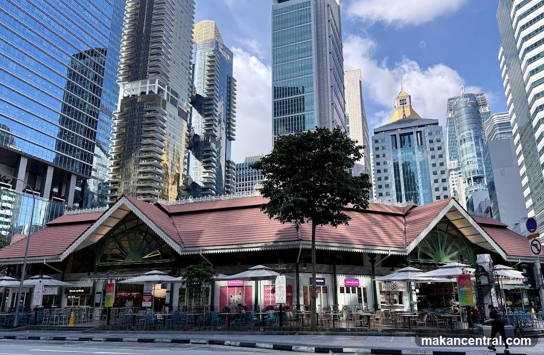 Outdoor seating area in front of a market building with skyscrapers in the background
