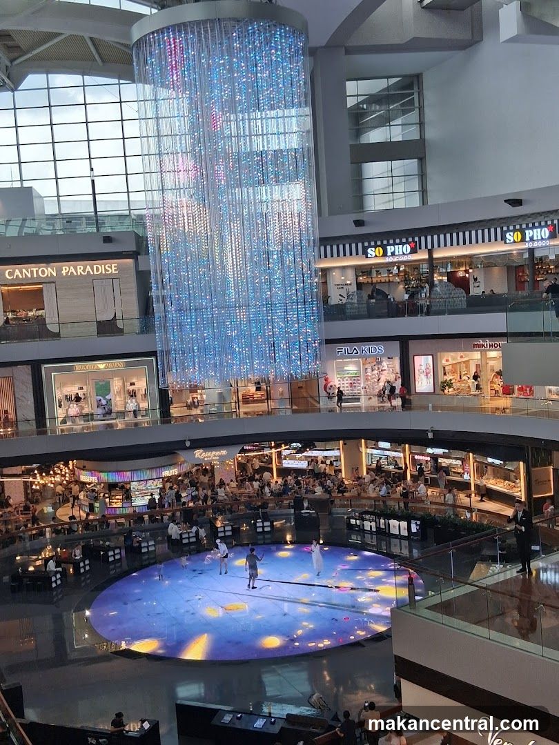 Indoor shopping mall atrium with a large crystal chandelier and a performance area
