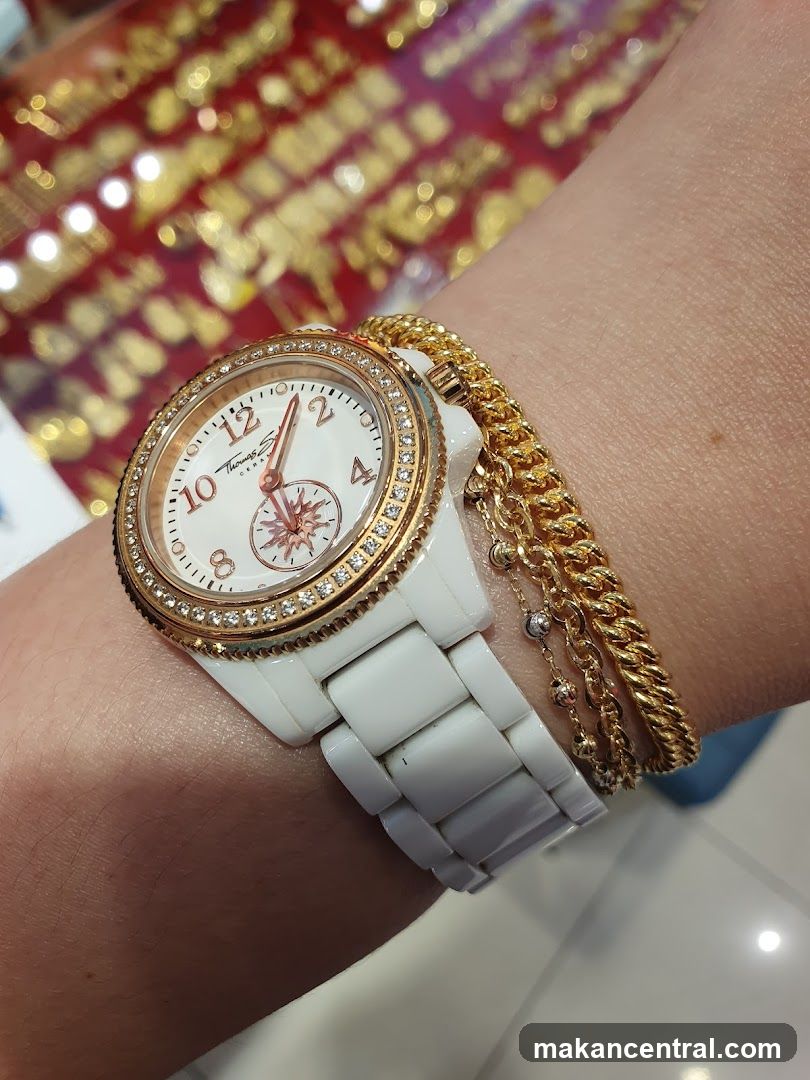 Woman wearing a white ceramic watch with gold accents and diamond embellishments, layered with gold bracelets.
