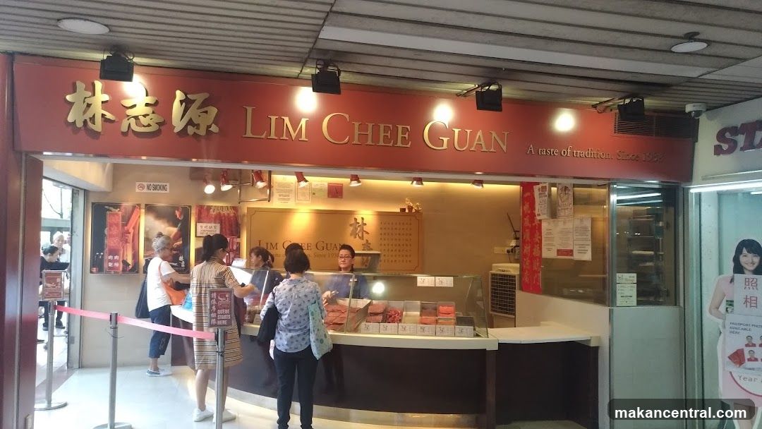 The exterior of a shop called Lim Chee Guan, with its name displayed prominently in gold lettering on a red background. The shop appears to sell food items, with display cases visible inside showing various products. Several customers are seen interacting with staff at the counter. A "No Smoking" sign is posted near the entrance. The shop's slogan "A taste of tradition. Since 1939" is also visible.