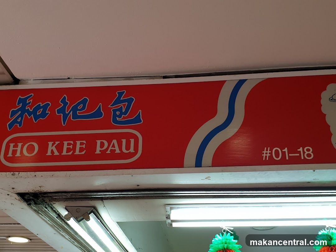 A red sign with blue Chinese characters and the English text "HO KEE PAU" is displayed above a storefront. The number "#01-18" is also visible on the sign. The sign appears to be part of the exterior of a business.