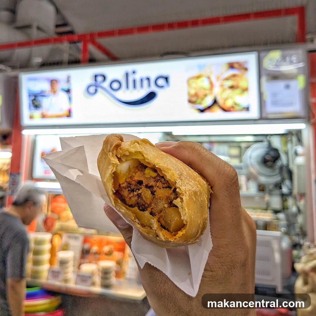 Hand holding a pastry in front of a food stall