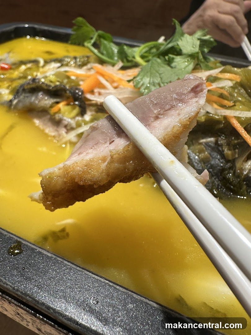 Close-up of a piece of meat being held by chopsticks over a dish of food.