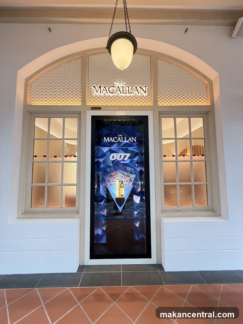 The exterior of a store with the prominent signage "THE MACALLAN" above an arched window. Below the signage is a display featuring "THE MACALLAN 007" with a bottle of whiskey. The store has two windows on either side of the central display.