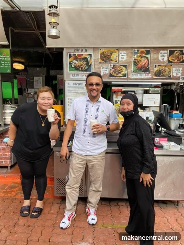 Three people posing in front of a food stall
