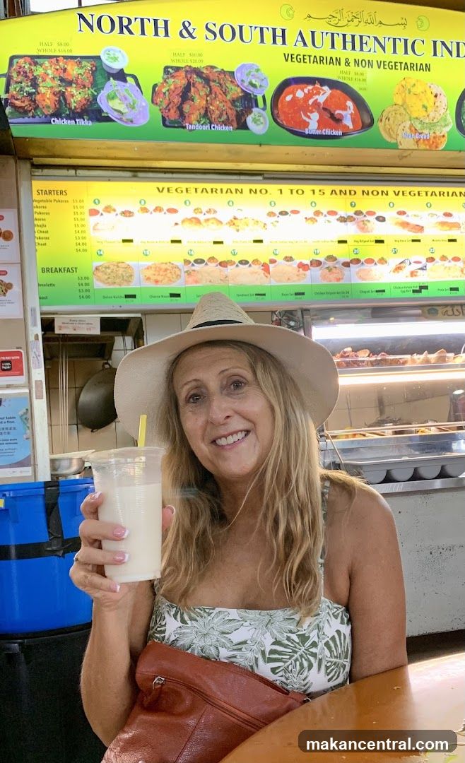 Woman holding a drink in front of an Indian food stall