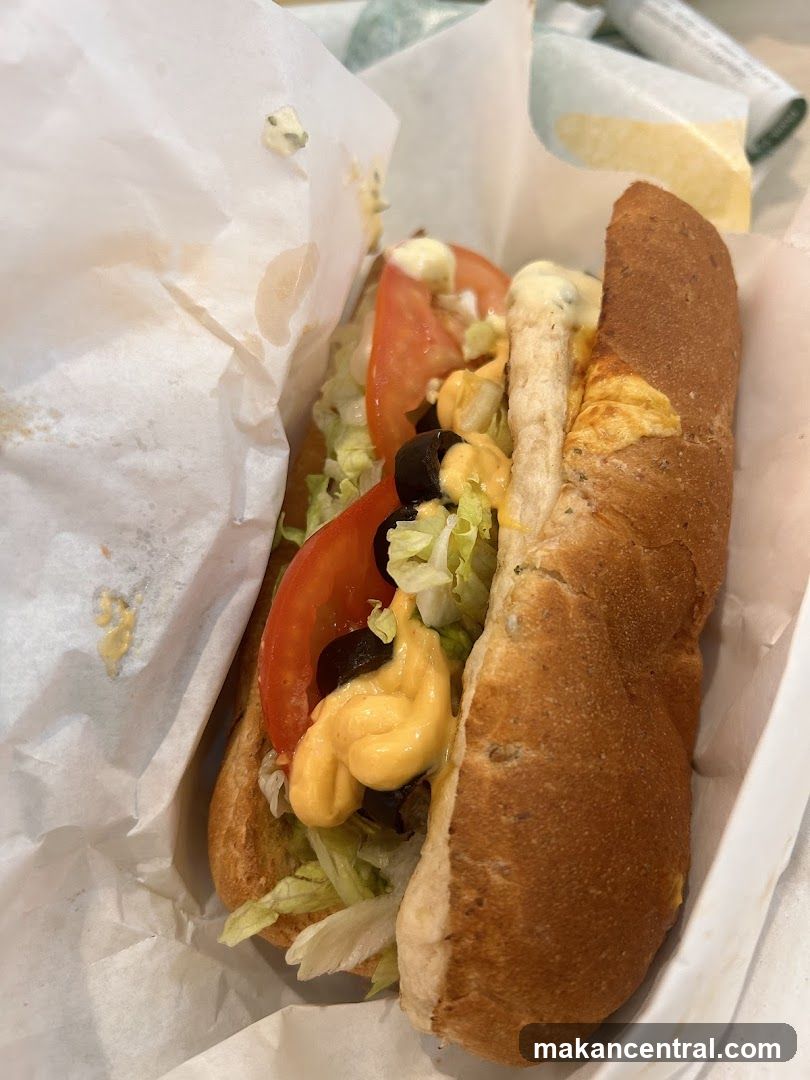 Sub sandwich with lettuce, tomato, olives, and cheese sauce