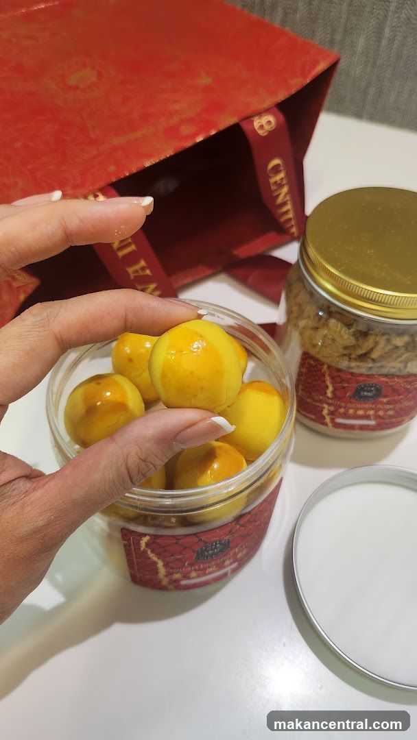 Hand holding golden-colored snacks with red packaging and a gold-lidded jar nearby