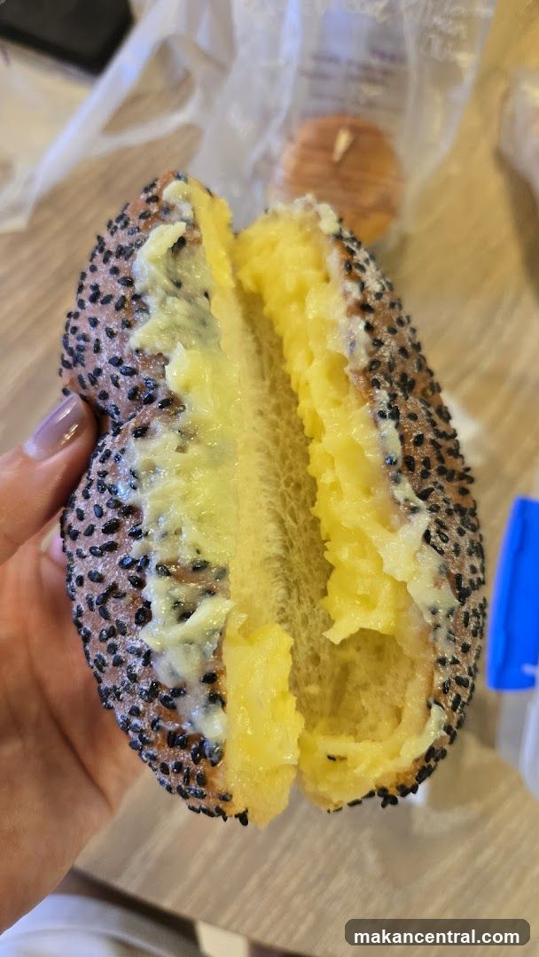 Hand holding a split-open sesame seed bun filled with yellow spread