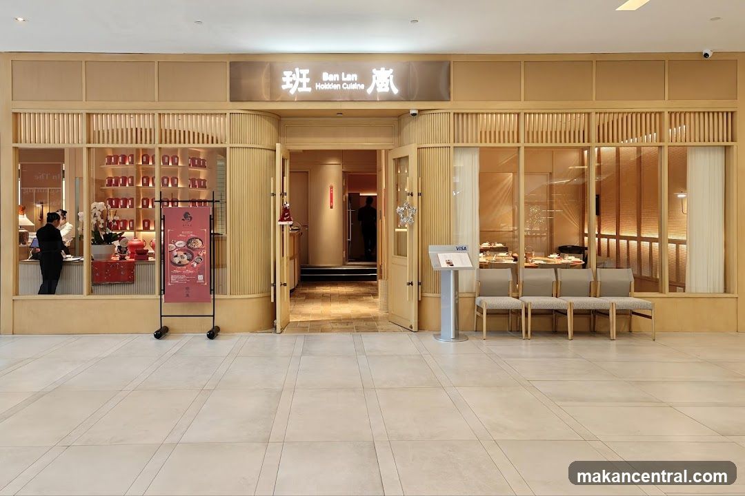 Modern wooden facade with illuminated sign displaying '班 Ben Lan 酒' above entrance. Glass windows show interior seating area and staff at counter. Open doorway leads to dining room. Promotional poster on stand outside is not part of shop front signage.