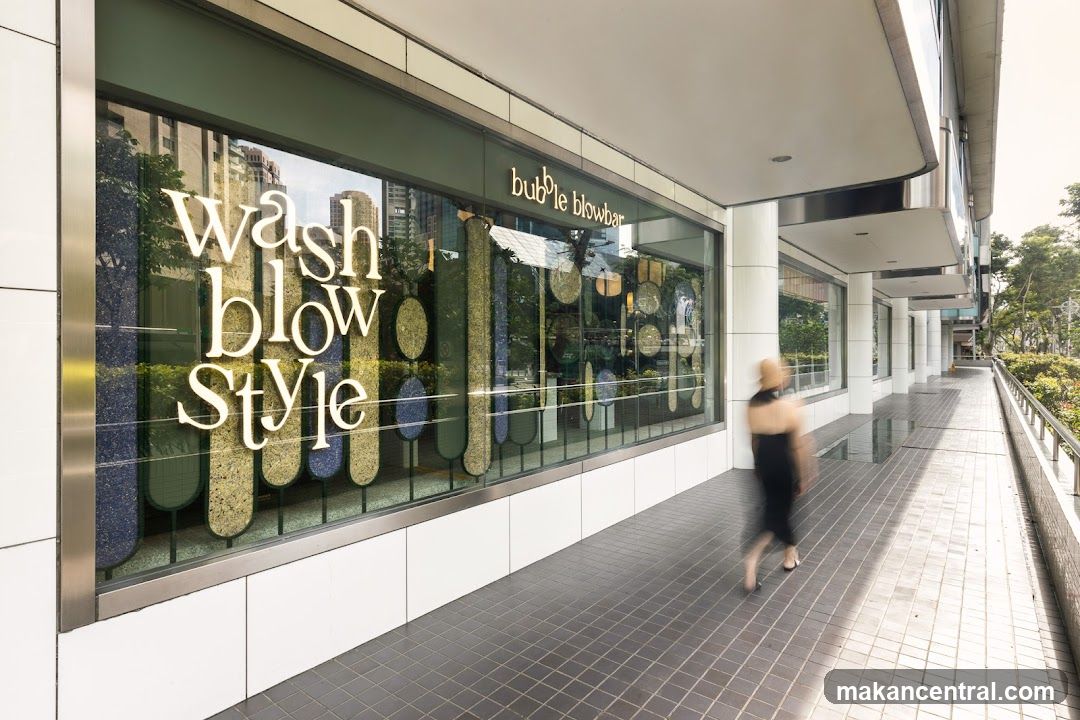 Exterior view of a modern retail storefront with large glass windows displaying the name 'Wash blow Style' in white lettering. Above the window, the shop's name 'bubble blowbar' is illuminated. The facade features clean lines, white panels, and a metallic trim. A pedestrian walks past on a tiled walkway under an overhang.
