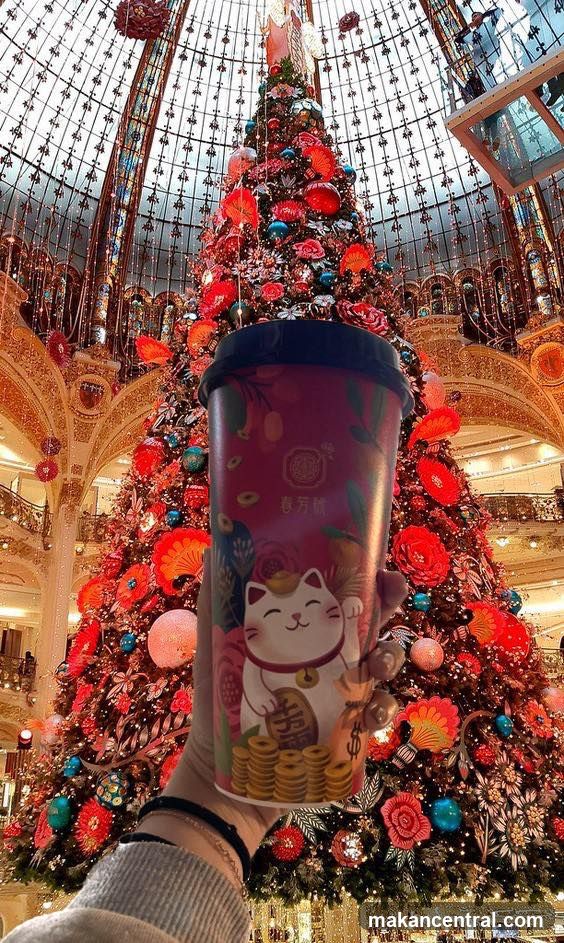 Hand holding beverage cup in front of Christmas tree