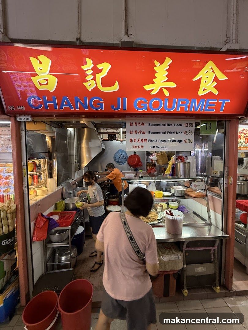 Red signboard with yellow Chinese characters '昌記美食' and blue English text 'CHANG JI GOURMET' above the entrance. Shopfront shows open kitchen area with staff working inside; customers are present at counter. Visible signage includes menu board listing items like 'Economical Bee Hoon', 'Economical Fried Mee', and 'Fish & Peanut Porridge'.