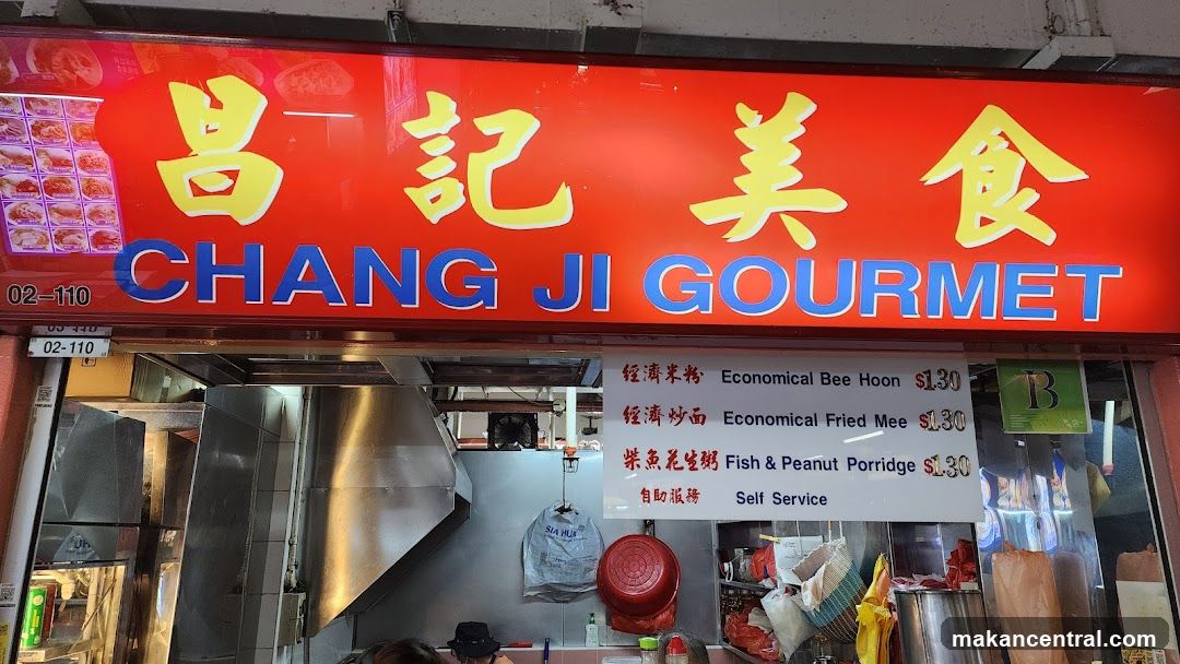 Exterior storefront with bright red sign featuring yellow Chinese characters '昌記美食' and blue English text 'CHANG JI GOURMET'. Below the main sign, a white menu board lists items like 'Economical Bee Hoon', 'Economical Fried Mee', and 'Fish & Peanut Porridge' priced at $1.30 each. The shop has stainless steel kitchen equipment visible inside, including a large vent hood and hanging bags. A small green 'B' sign is on the right side.