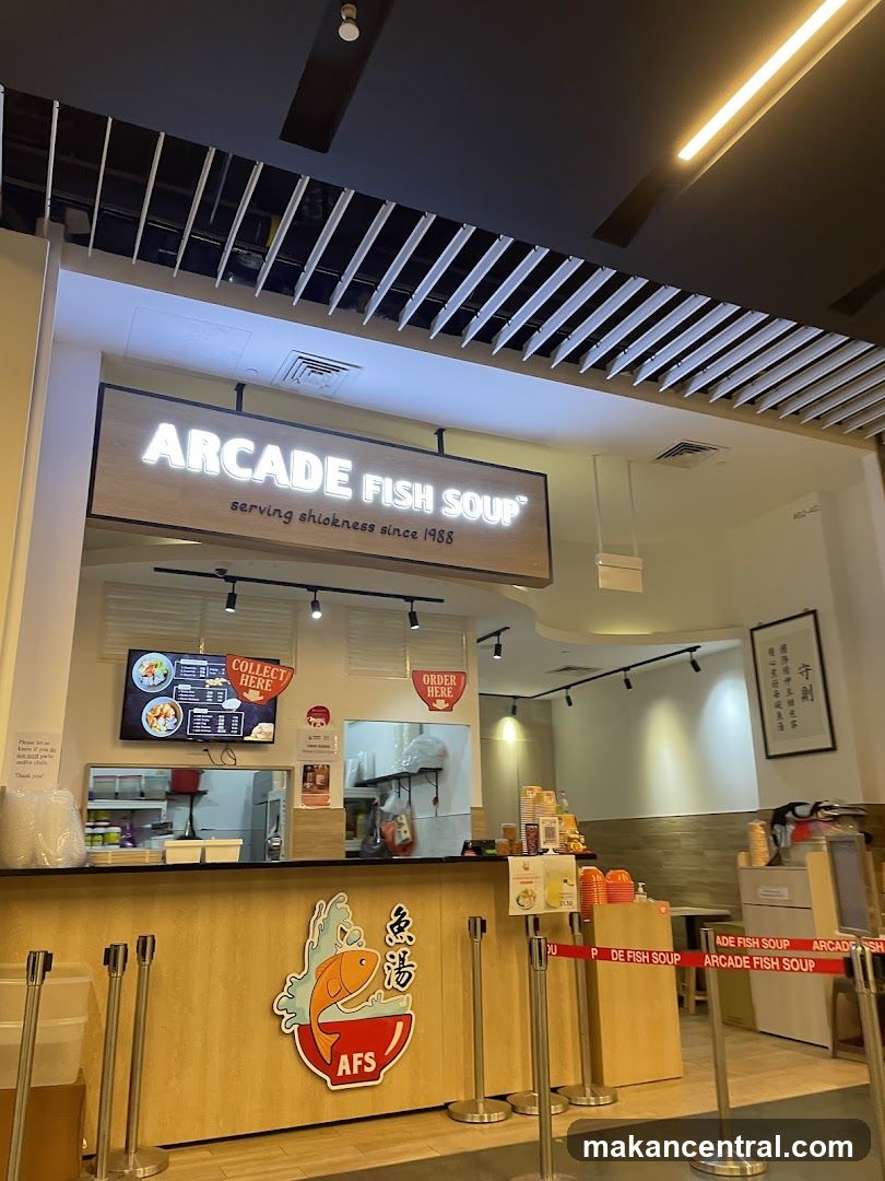 The storefront of a restaurant called Arcade Fish Soup, which has been serving since 1988. The sign above the counter reads "ARCADE FISH SOUP serving shiokness since 1988". There are signs for "COLLECT HERE" and "ORDER HERE". The counter has a logo with a fish and Chinese characters.