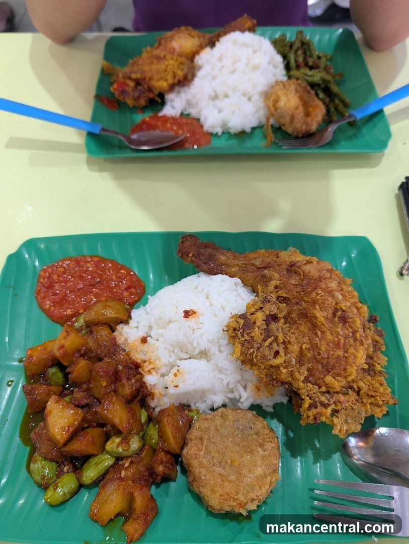 Two plates of rice with fried chicken and side dishes