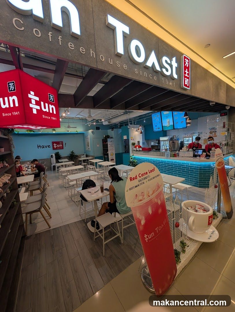 The exterior of a Fun Toast coffeehouse with prominent signage. Inside, tables and chairs are set up, and staff can be seen behind the counter. A large promotional cutout of a drink is displayed in the foreground.
