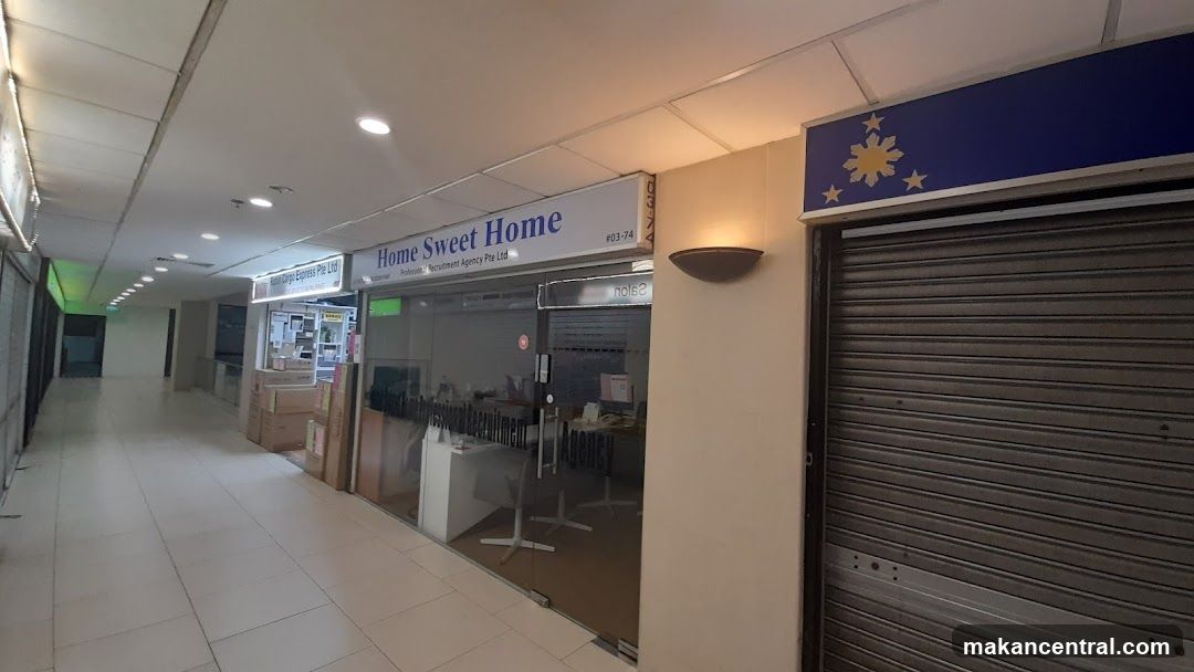 The exterior of a recruitment agency with a glass storefront. The sign above reads "Home Sweet Home" and "Recruitment Agency Pte Ltd". There is a closed metal shutter to the right of the agency.